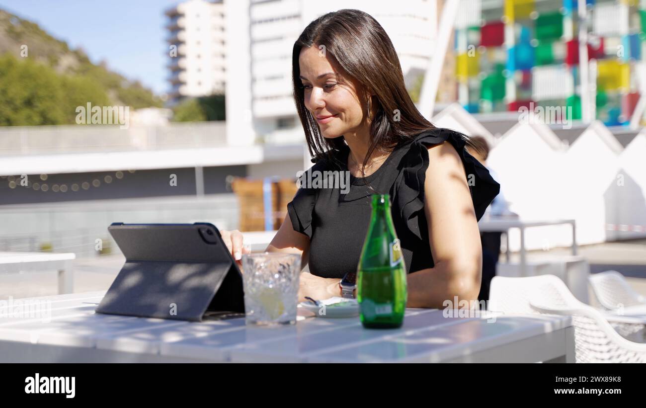 Une femme élégante utilise une tablette à une table de café en plein air avec une boisson rafraîchissante en Espagne. Banque D'Images