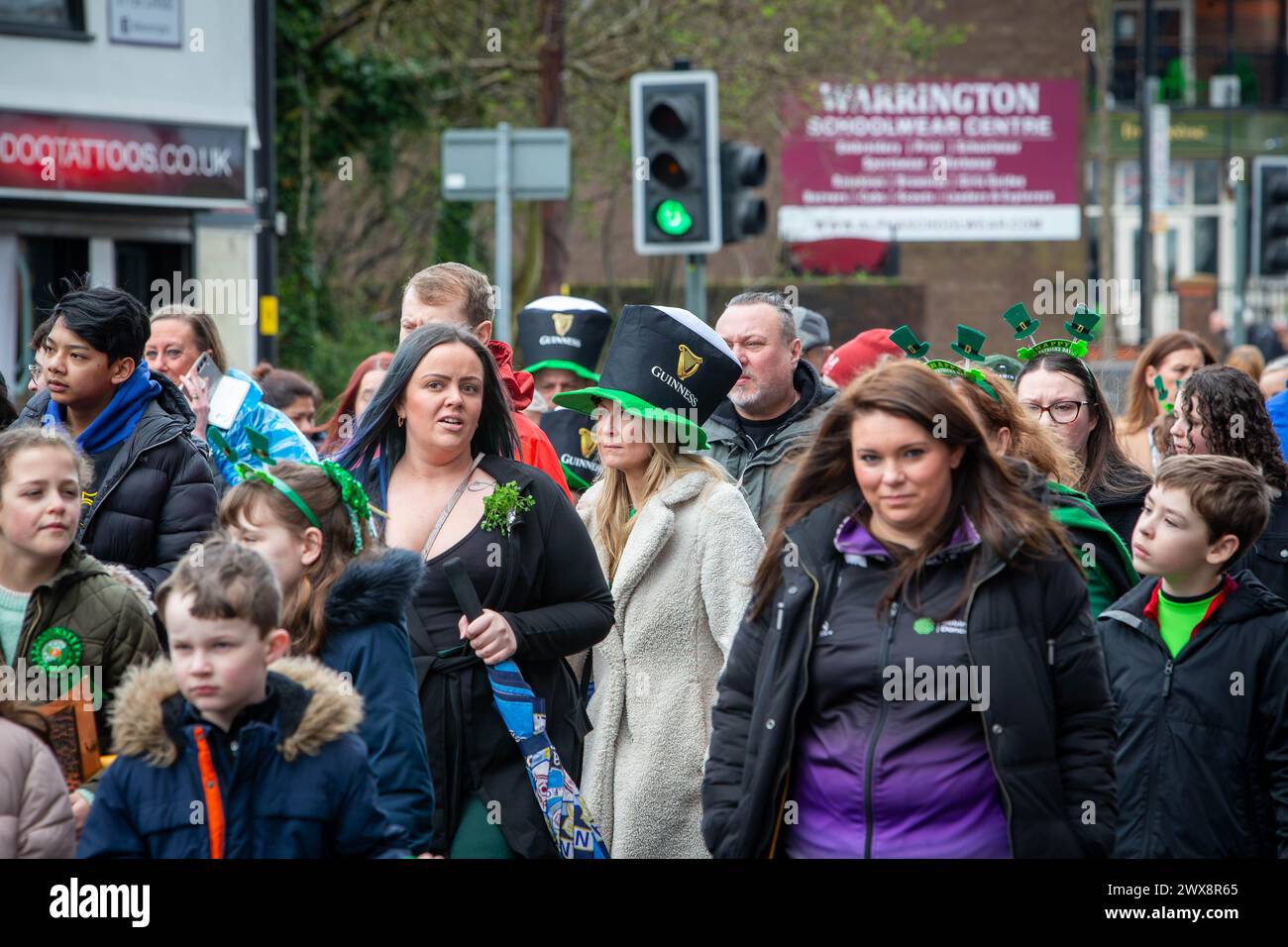 Une dame blonde portant un chapeau Guinness marche avec la foule pendant la parade de la St Patrick de Warrington en 2024 Banque D'Images