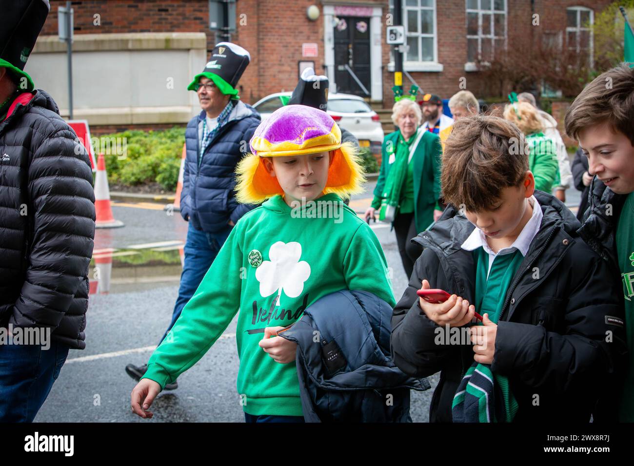 Garçon portant un chapeau violet avec des cheveux jaunes regarde son ami au téléphone dans la parade de la St Patrick de Warrington en 2024 Banque D'Images