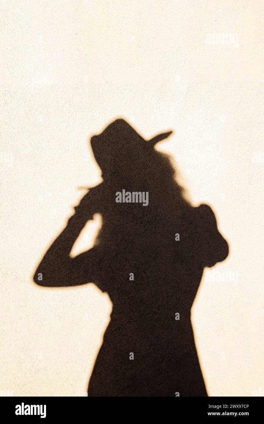Ombre abstraite d'une femme portant un chapeau reflet sur le mur à la lumière du coucher du soleil Banque D'Images