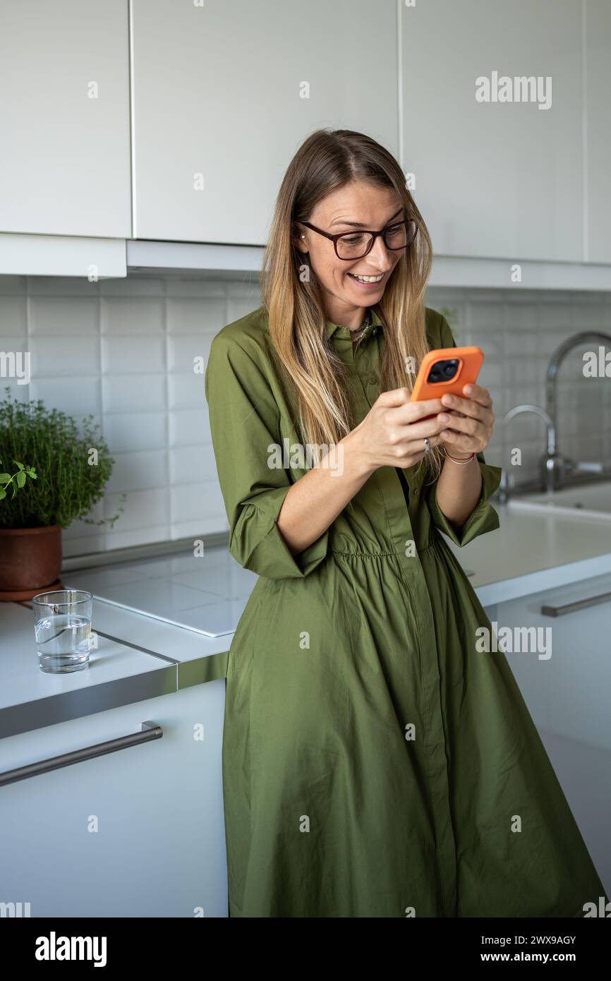 Heureuse surprise femme satisfaite souriante lisant des messages discutant dans les médias sociaux de smartphone à la maison Banque D'Images