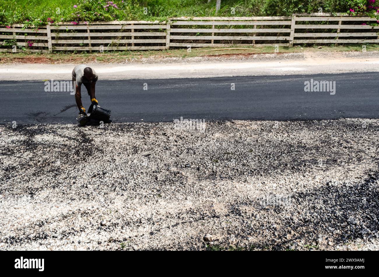 Un homme sur un projet de rétrécissement routier verse de l'huile noire d'un seau noir dans un récipient plus petit. Banque D'Images