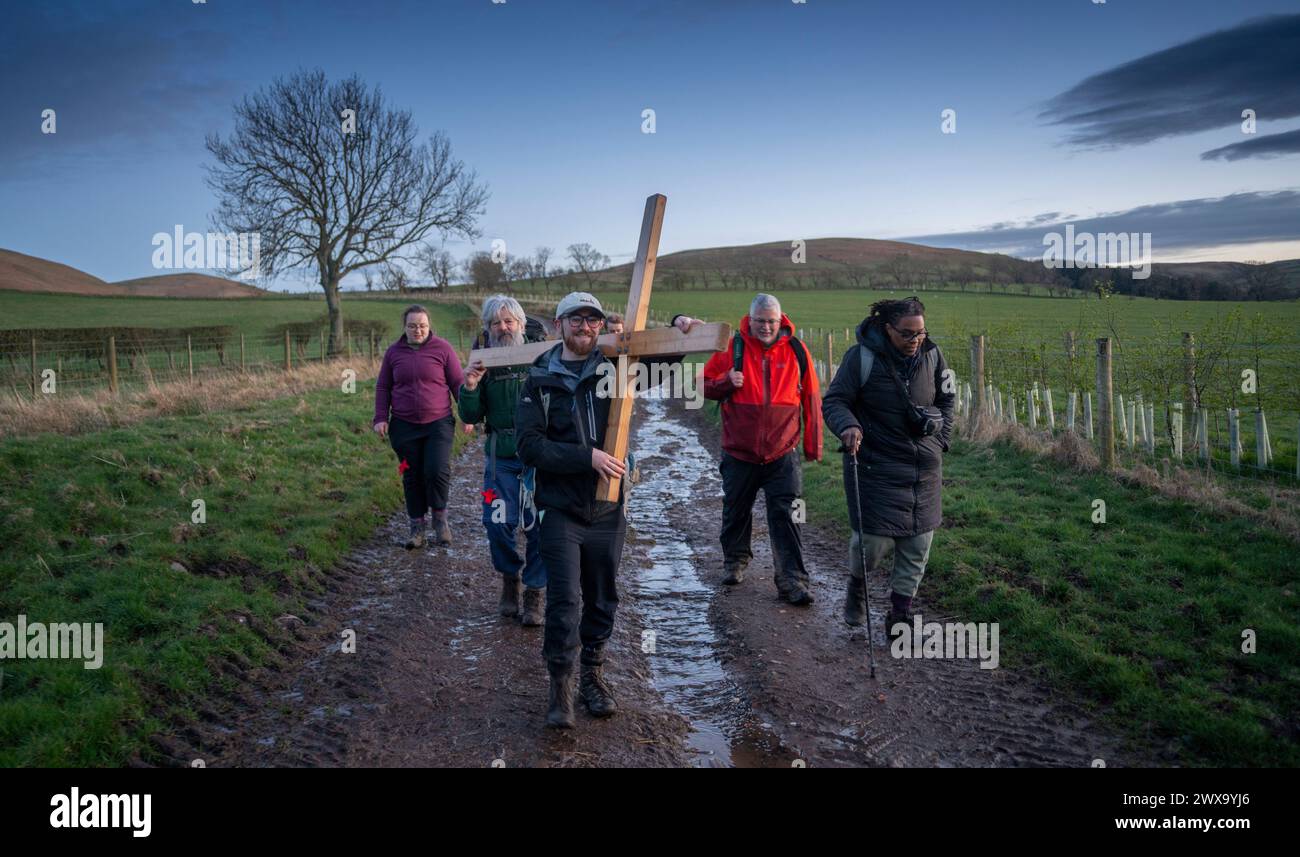 Ingham, Royaume-Uni. 27 mars 2024. Ingham, Northumberland, Angleterre. Northern Cross Pilgrims Pictures alors qu'ils arrivent au crépuscule à Ingham, Northumberland, le groupe marchant portant une grande croix en bois de Carlisle en Cumbria, à Beal en Northumberland, où ils se rassemblent le vendredi Saint pour traverser les appartements à marée basse pour la dernière étape à travers l'île Sainte de Lindisfarne pour célébrer Pâques. Crédit photos : phil wilkinson/Alamy Live News Banque D'Images