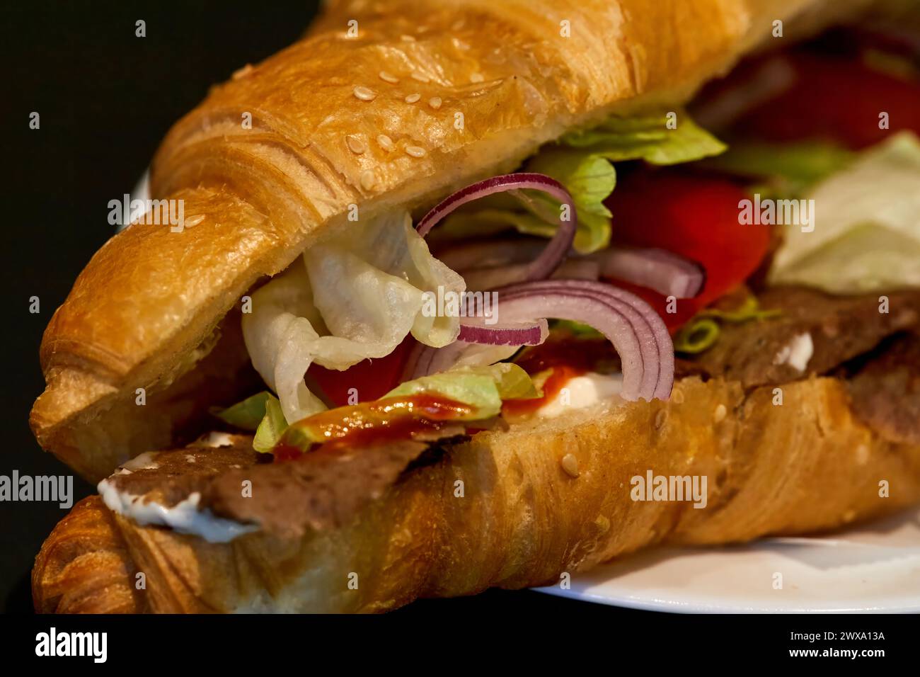 Image de rondelles d'oignon, de laitue et de tomates dans un croissant avec de la viande et de la sauce Banque D'Images