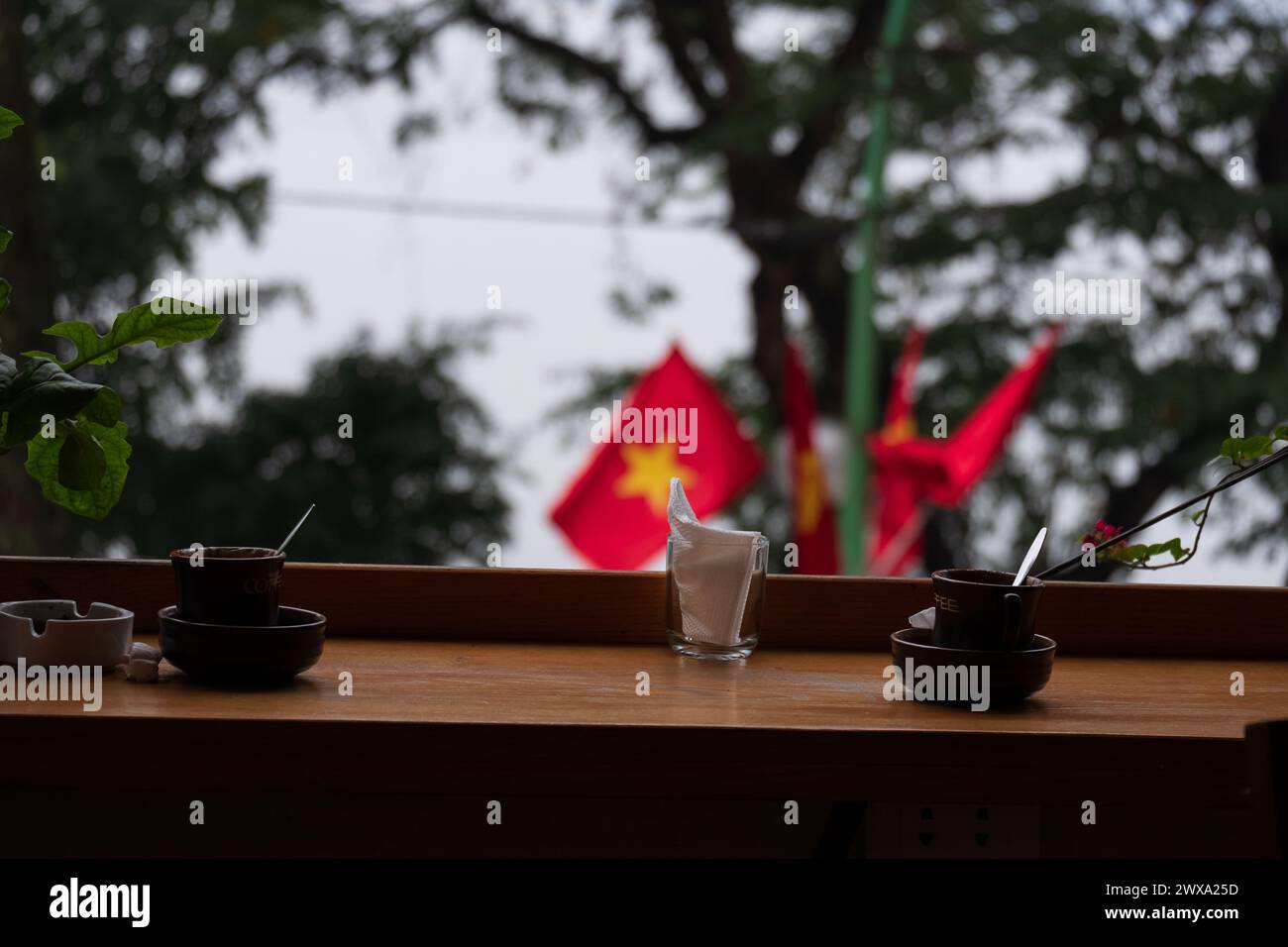 Sur un toit-terrasse surplombant la ville, les tasses à café occupent le devant de la scène avec un drapeau vietnamien flottant en toile de fond Banque D'Images