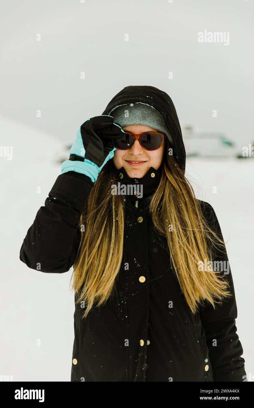 Fille en vêtements d'hiver entourée de neige souriant à la caméra Banque D'Images
