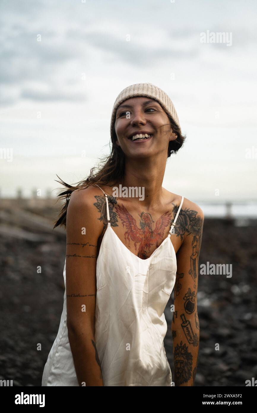 Jeune femme heureuse tatouée dans une robe sur une plage rocheuse venteuse. Banque D'Images