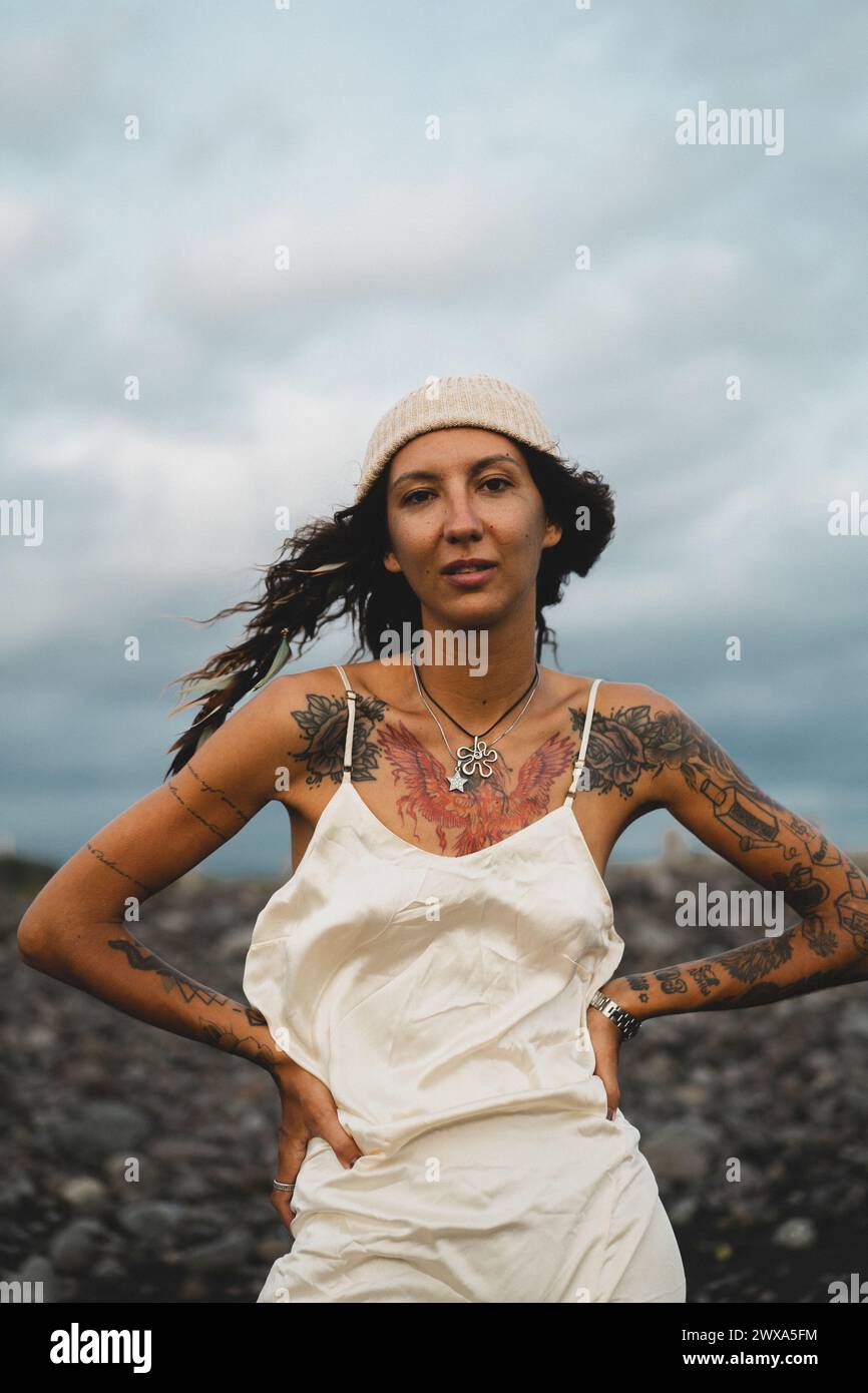 Jeune femme heureuse tatouée dans une robe sur une plage rocheuse venteuse. Banque D'Images