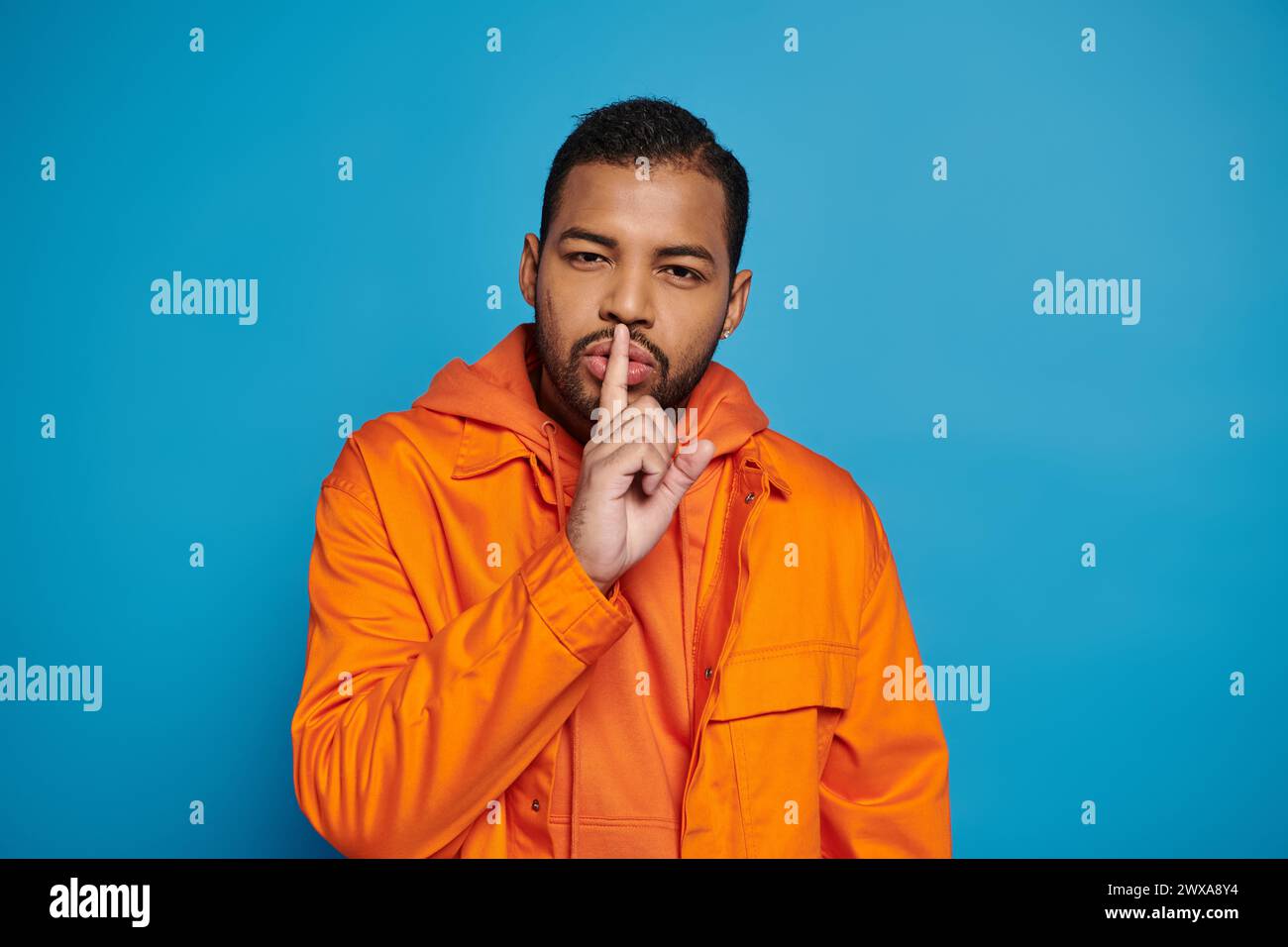 attrayant homme afro-américain en tenue orange montrant le silence de geste de hush sur fond bleu Banque D'Images