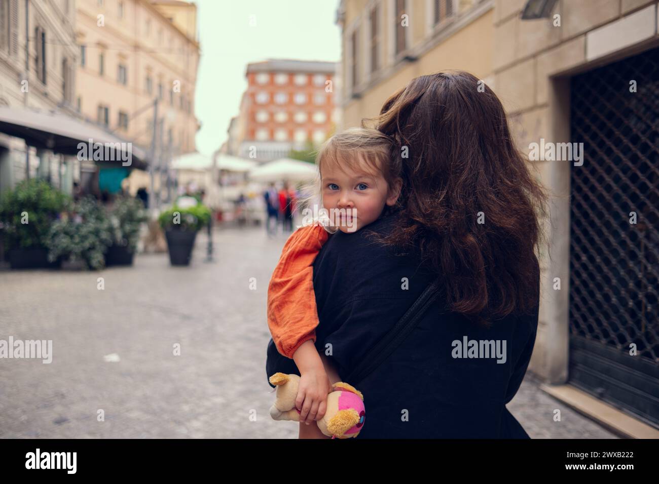 Maman porte sa fille dans ses bras. Une petite fille est assise dans les bras de sa mère et sourit doucement. Maman et fille marchent dans la rue d'un beau Banque D'Images