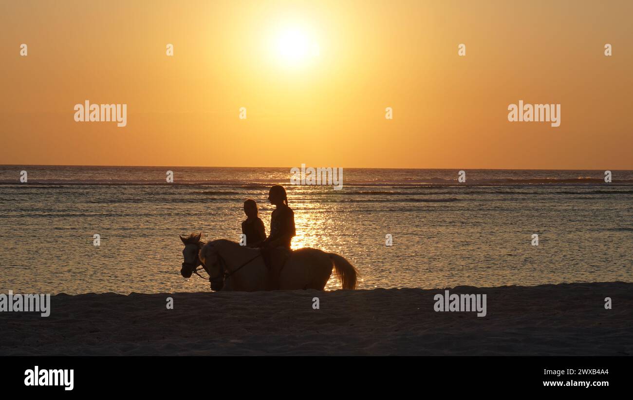 Les gens qui montent à cheval sur la plage au coucher du soleil sur l'île Gili Trawangan, Lombok Banque D'Images