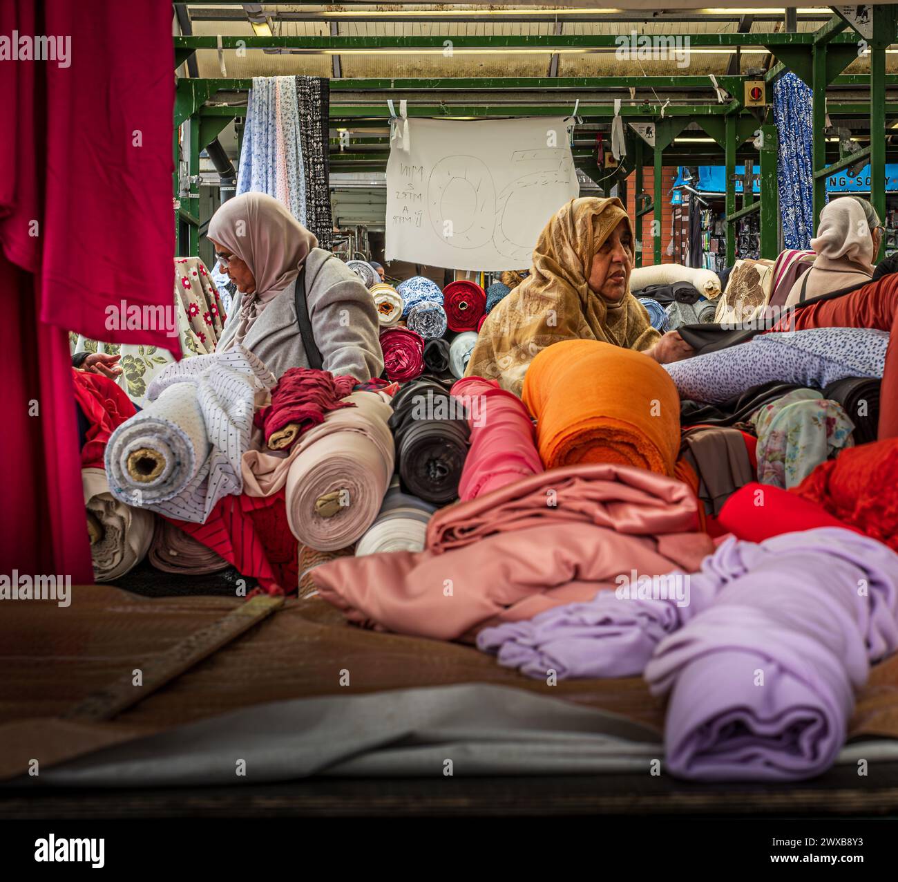 Dames musulmanes portant des foulards achetant du tissu et du matériel à partir de rouleaux de matériel sur un stand de marché en plein air Banque D'Images