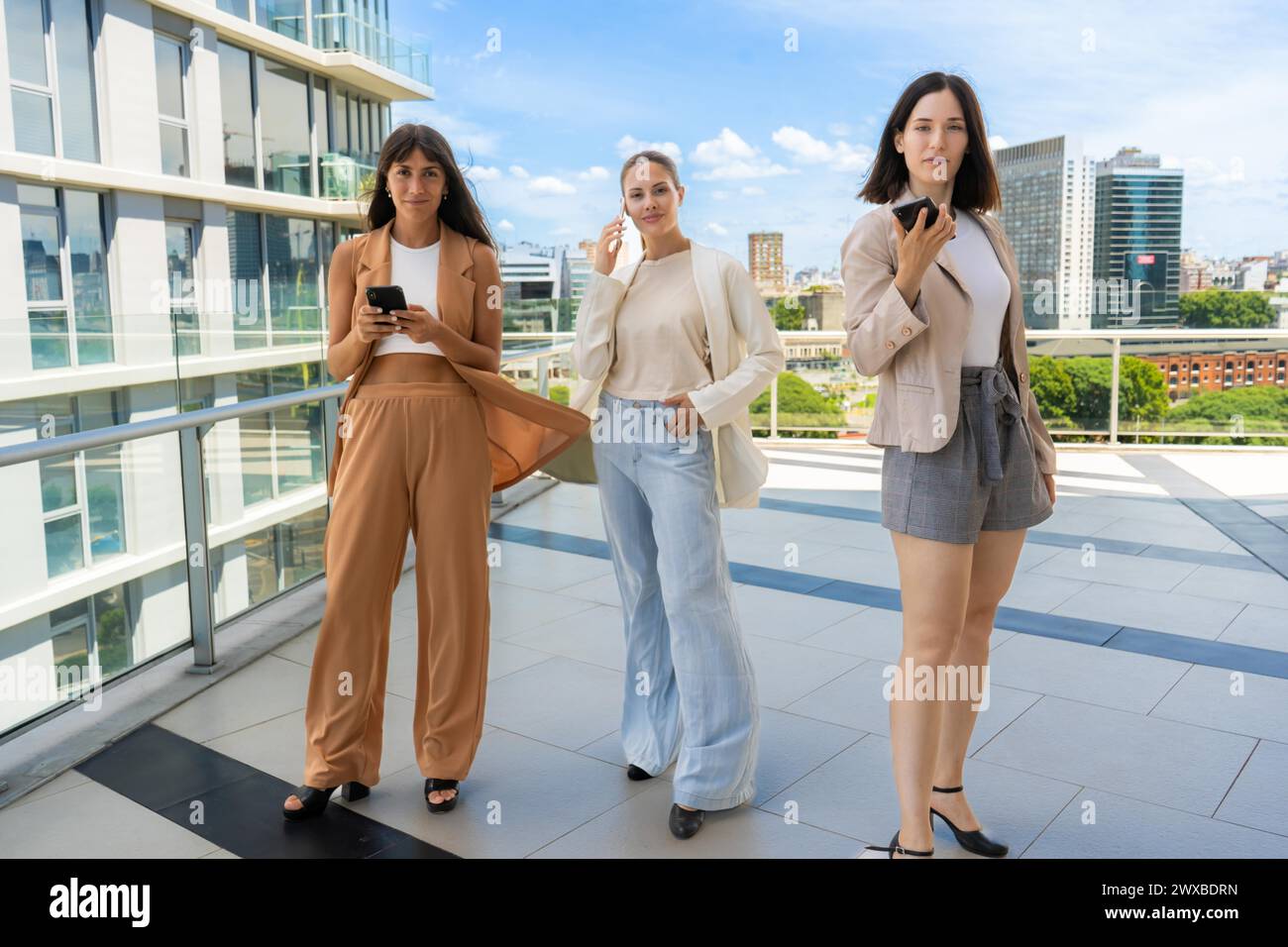 Trois femmes d'affaires tenant des smartphones regardent l'appareil photo tout en posant pour la photo Banque D'Images