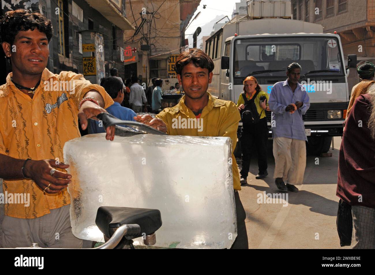 Deux hommes soulevant un gros bloc de glace dans un marché animé, Rajasthan, Inde du Nord, Inde Banque D'Images