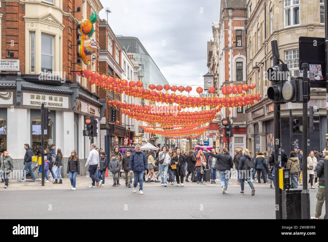 L'agitation des gens dans Wardour Street à l'entrée de Chinatown, Londres. Surveillé et accueilli par la sculpture emblématique du lion chinois. Banque D'Images