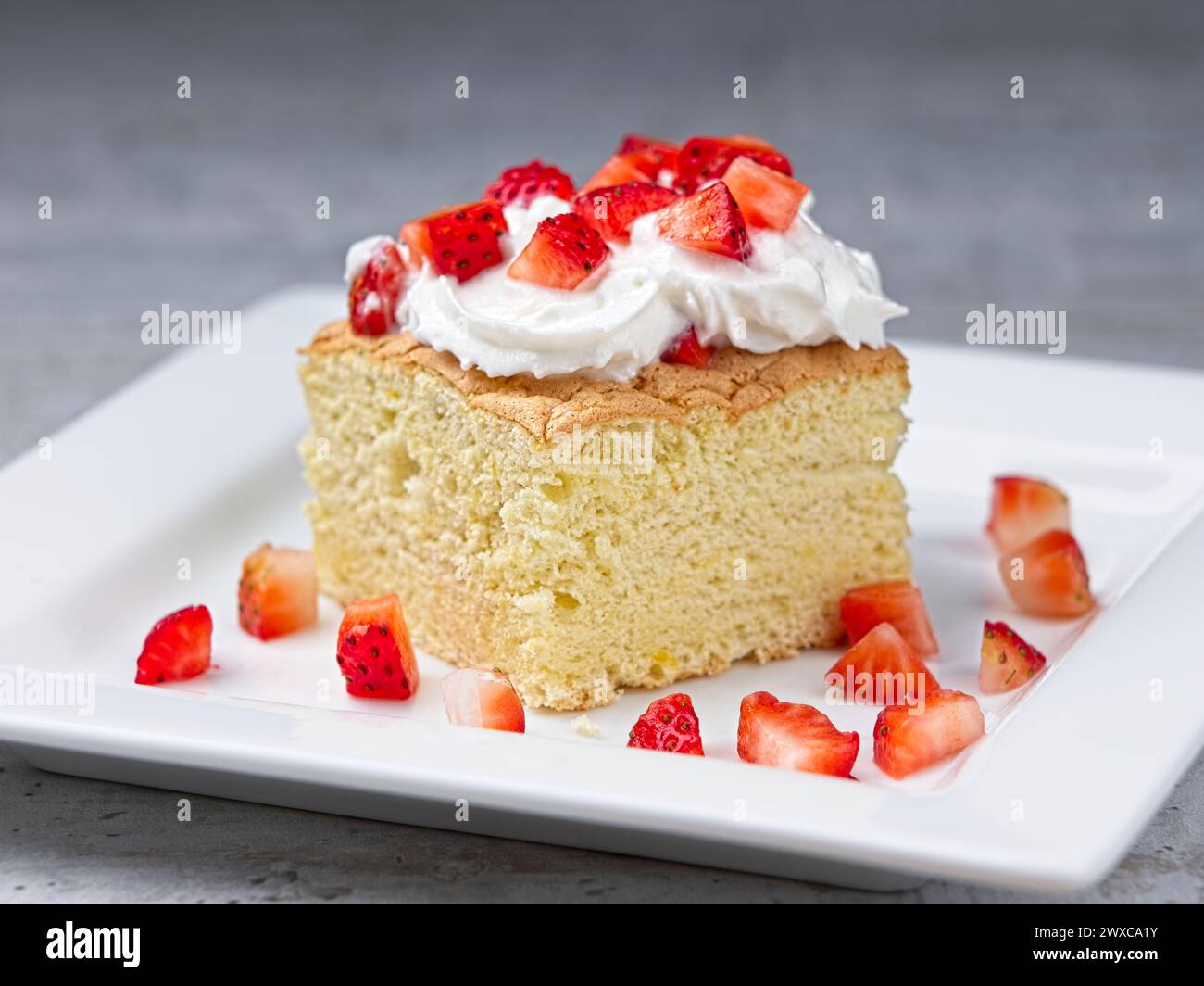 Une photo rapprochée d'une tranche de gâteau éponge maison garnie de crème fouettée et de srtawberries coupées. Banque D'Images