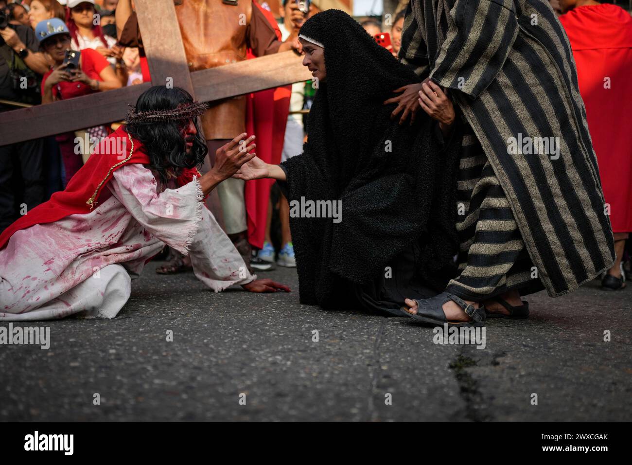 A devotee playing the role of the Virgin Mary offers her hand to a penitent depicting the role of Jesus Christ during a Way of the Cross reenactment, as part of Holy Week celebrations in the Petare neighborhood of Caracas, Venezuela, Friday, March 29, 2024. Holy Week commemorates the last week of the earthly life of Jesus Christ culminating in his crucifixion on Good Friday and his resurrection on Easter Sunday. (AP Photo/Matias Delacroix) Banque D'Images