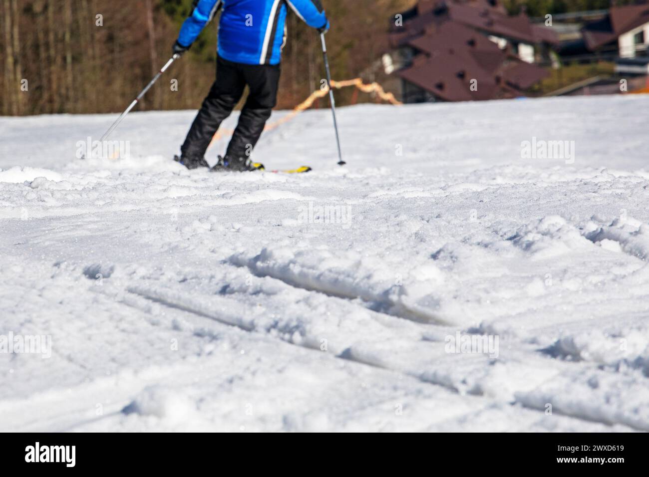 skieur en veste bleue part d'une pente enneigée par une journée ensoleillée. Vacances actives en famille Banque D'Images