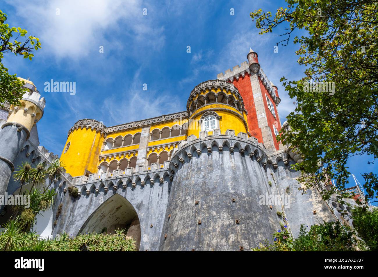 Vue en bas angle sur les murs fortifiés du Palais de Pena dans un style coloré jaune et rouge sur les murs recouverts de quelques palmiers sous un bleu ensoleillé s. Banque D'Images