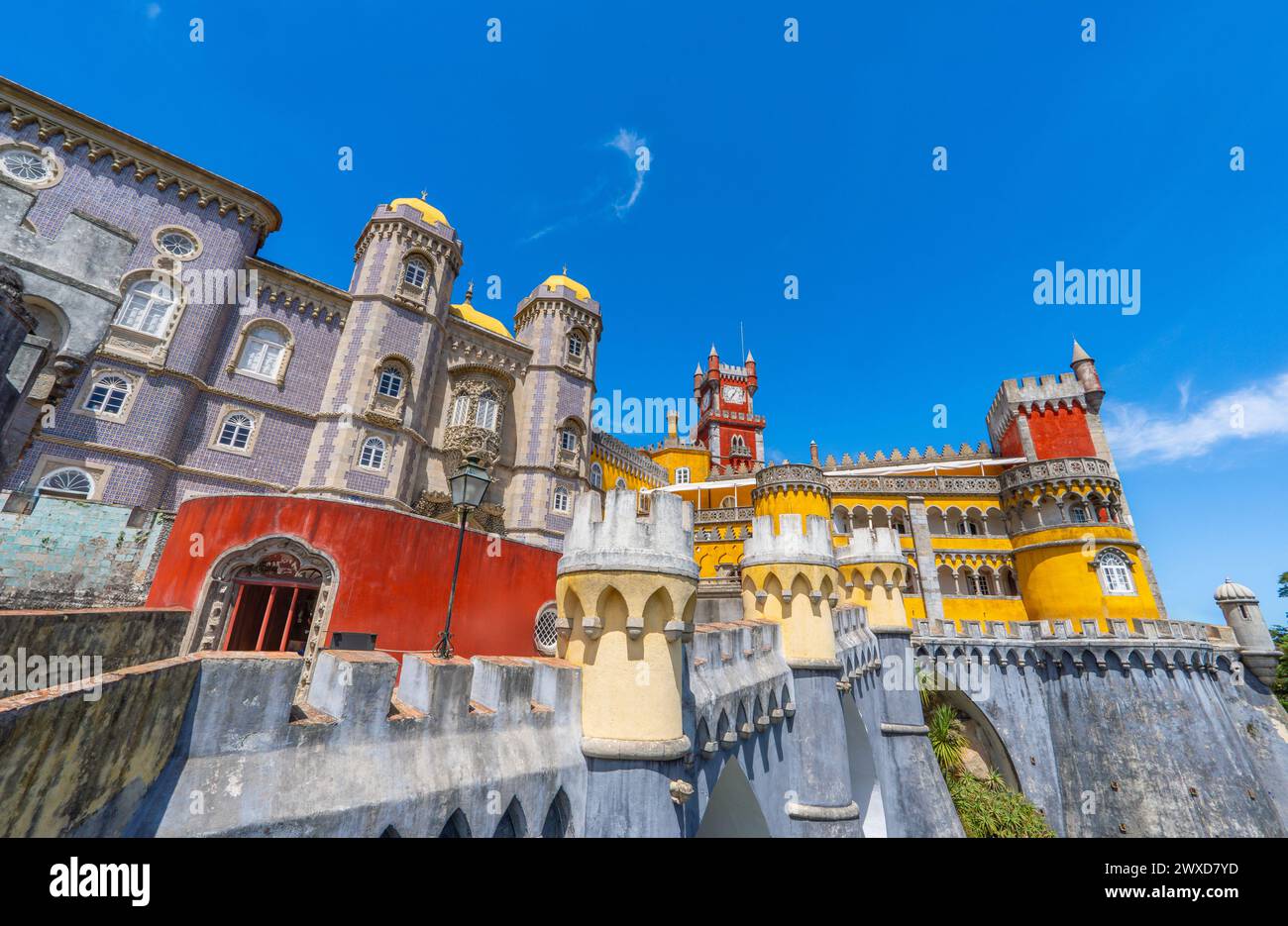 Vue extérieure grand angle du Palais de Pena avec des murs de couleur jaune et rouge et des mosaïques sur le mur et les murs fortifiés, sous un ciel bleu ensoleillé. Sintra Banque D'Images
