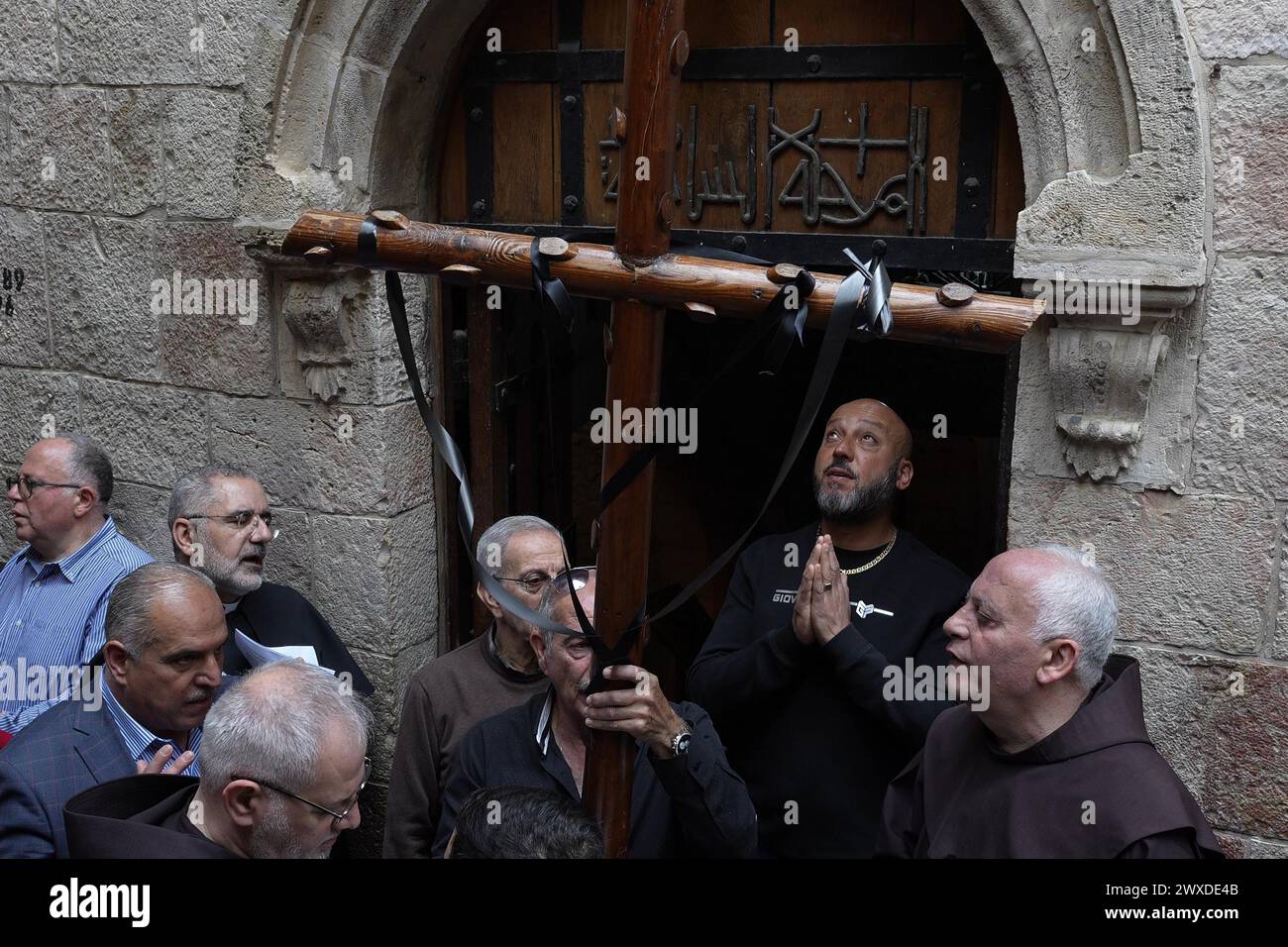 Les fidèles arabes chrétiens prient et se tiennent debout avec une grande croix en bois à la 6ème station de la croix alors qu’ils prennent part à la procession du chemin de croix le long de la via Dolorosa pendant la semaine Sainte de Pâques le 29 mars 2024 à Jérusalem. Les chrétiens célèbrent le vendredi Saint pour commémorer la crucifixion de Jésus et sa mort sur la croix. Banque D'Images