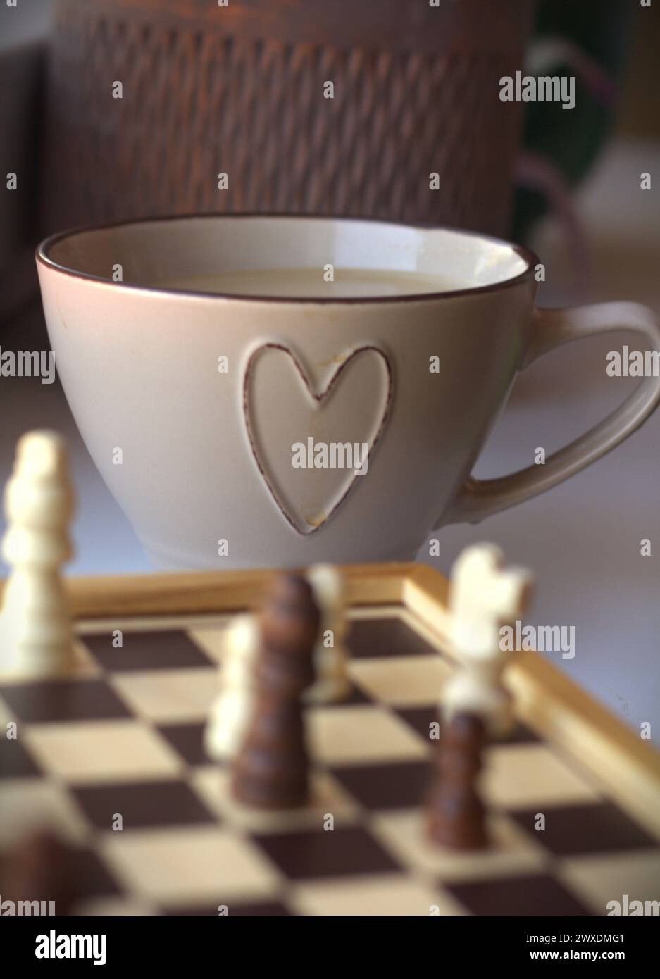 Jeu d'échecs - échiquier avec les pièces d'échecs et une tasse à café décorée avec un symbole de coeur Banque D'Images