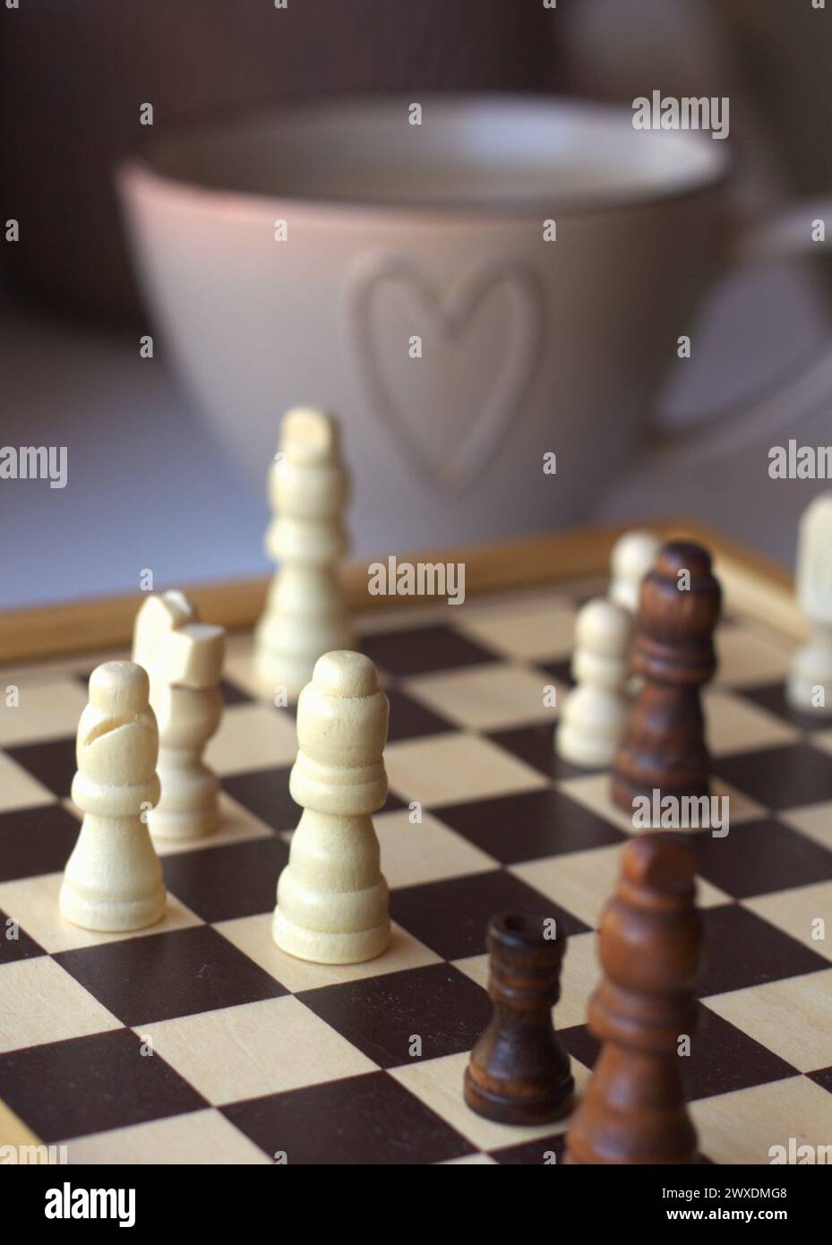 Jeu d'échecs - échiquier avec les pièces d'échecs et une tasse à café décorée avec un symbole de coeur Banque D'Images