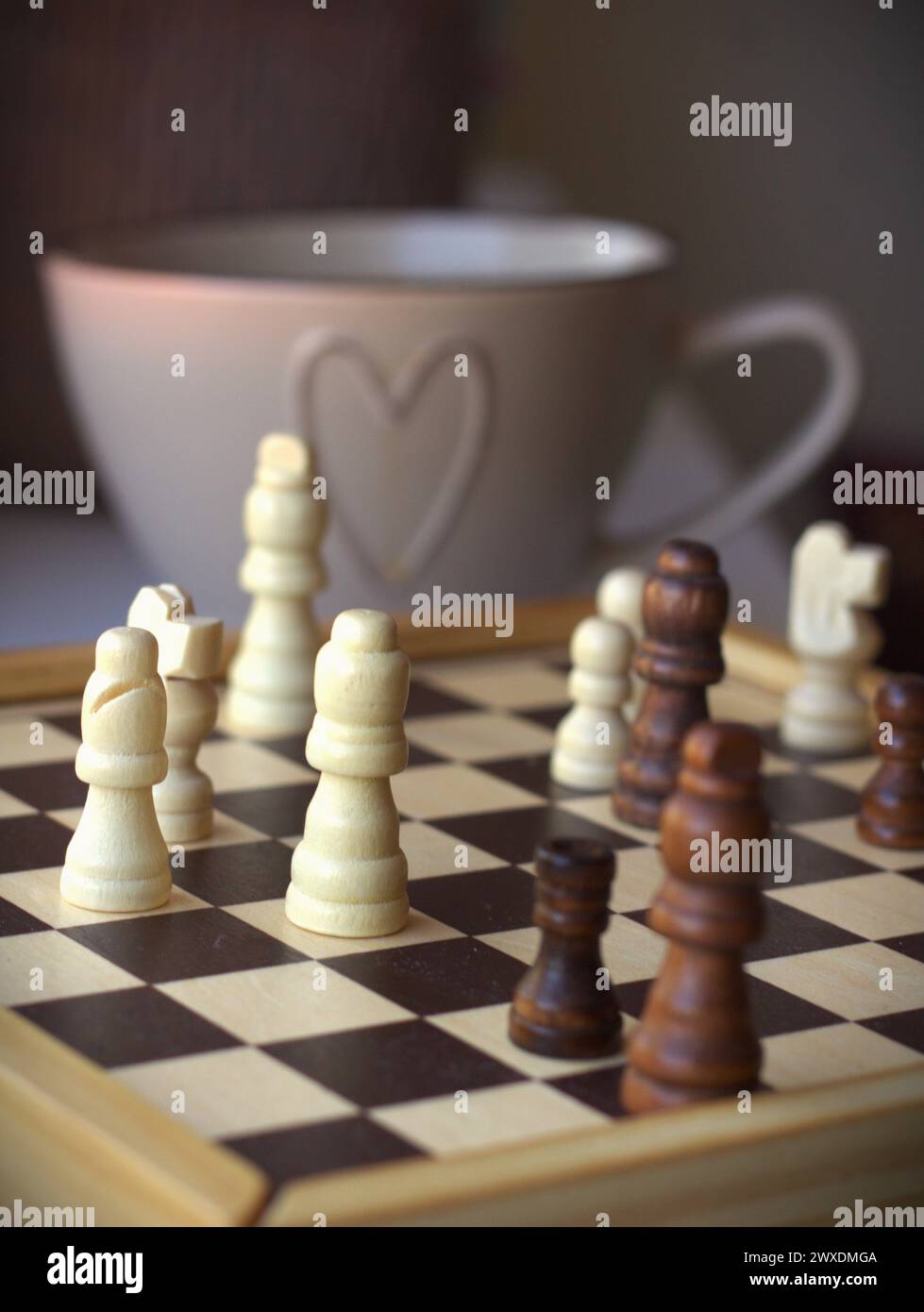 Jeu d'échecs - échiquier avec les pièces d'échecs et une tasse à café décorée avec un symbole de coeur Banque D'Images