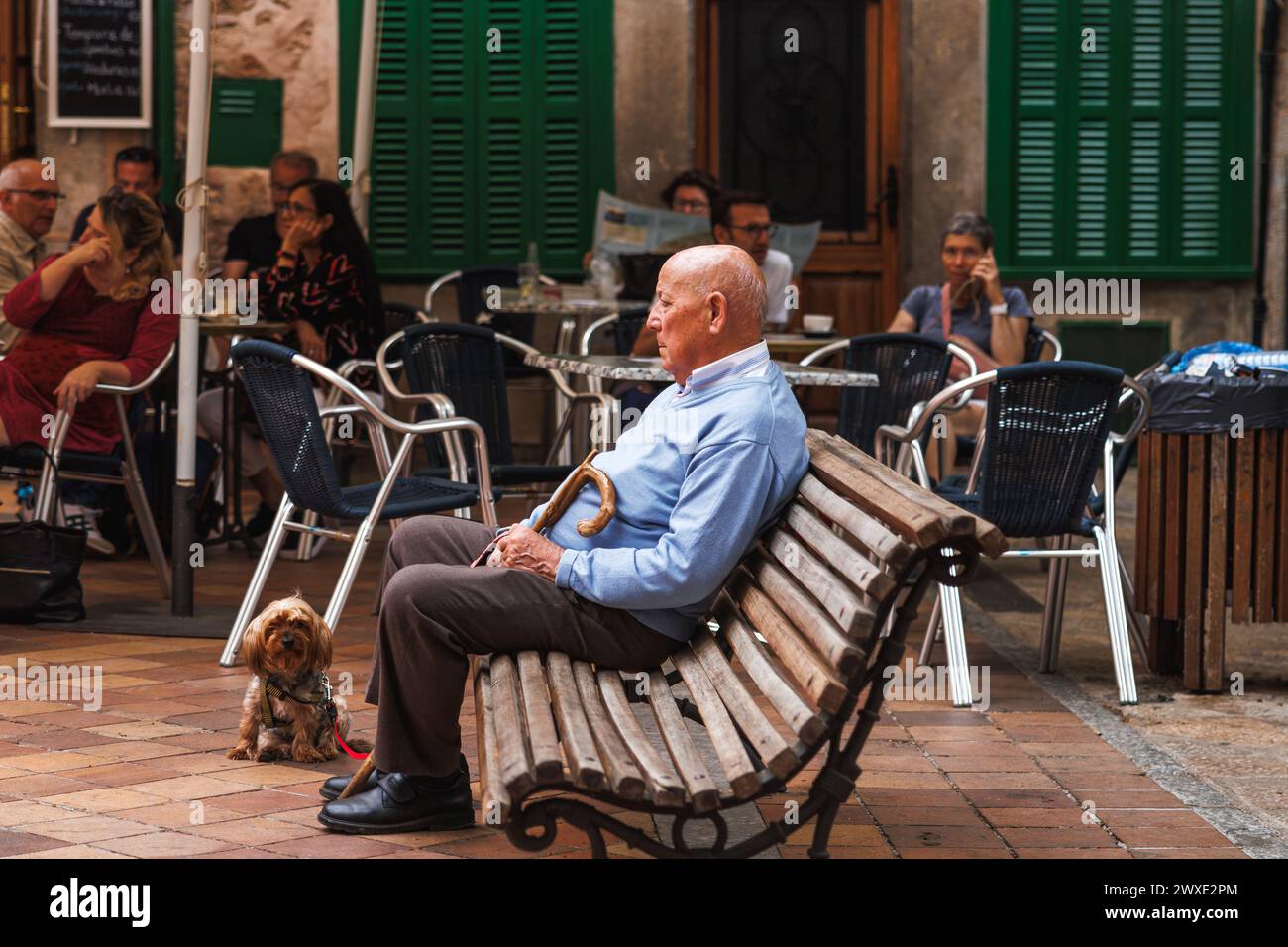 Fornalutx, Majorque, Espagne - 7 mai 2023 : un homme âgé avec son chien se repose sur un banc dans un village de montagne typique près d'un café. Contraste de paisible Banque D'Images