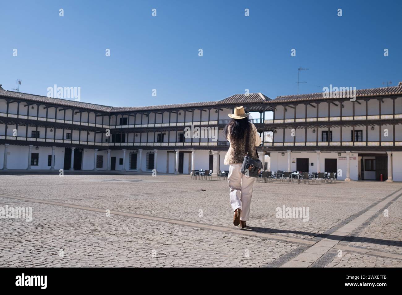 D'en bas, une voyageuse anonyme d'âge moyen vêtue d'un gilet et d'un chapeau de cow-boy, marchant sur une place historique. Sur la Plaza Mayor de Tembleque à Tolède Banque D'Images