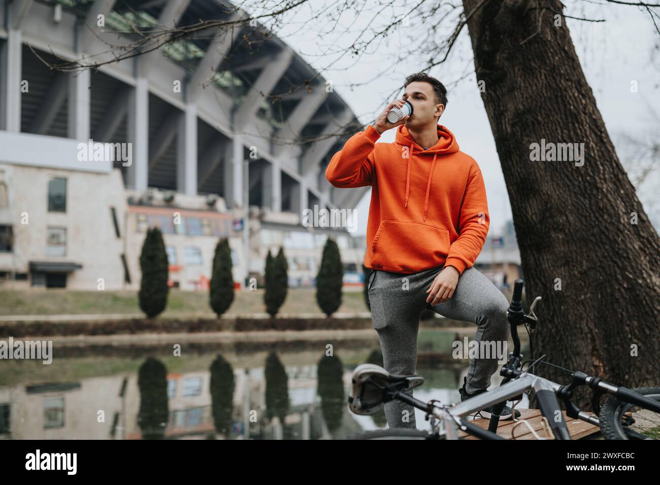 Jeune homme profitant d'une pause café paisible dans le parc avec son vélo par un jour nuageux Banque D'Images