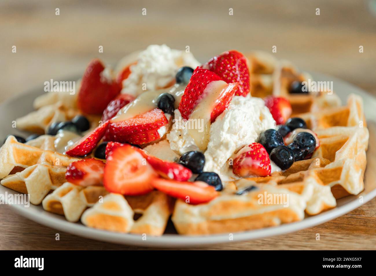Gaufres belges dorées garnies de fraises, de myrtilles et de crème fraîchement fouettée. Un délice appétissant à chaque bouchée pour un petit déjeuner spécial. Banque D'Images
