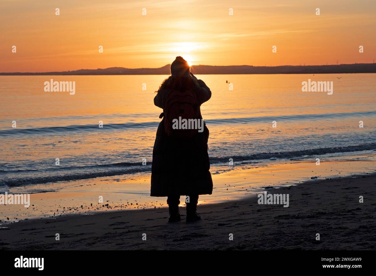 Portobello, Édimbourg, Écosse, Royaume-Uni. 31 mars 2024. Magnifique lever de soleil pour accueillir en été britannique sur le bord de mer écossais, ainsi que le dimanche de Pâques. Photo : une femme se tient sur le rivage en train de prendre une photo du lever du soleil. Credit : Arch White/Alamy Live news. Banque D'Images