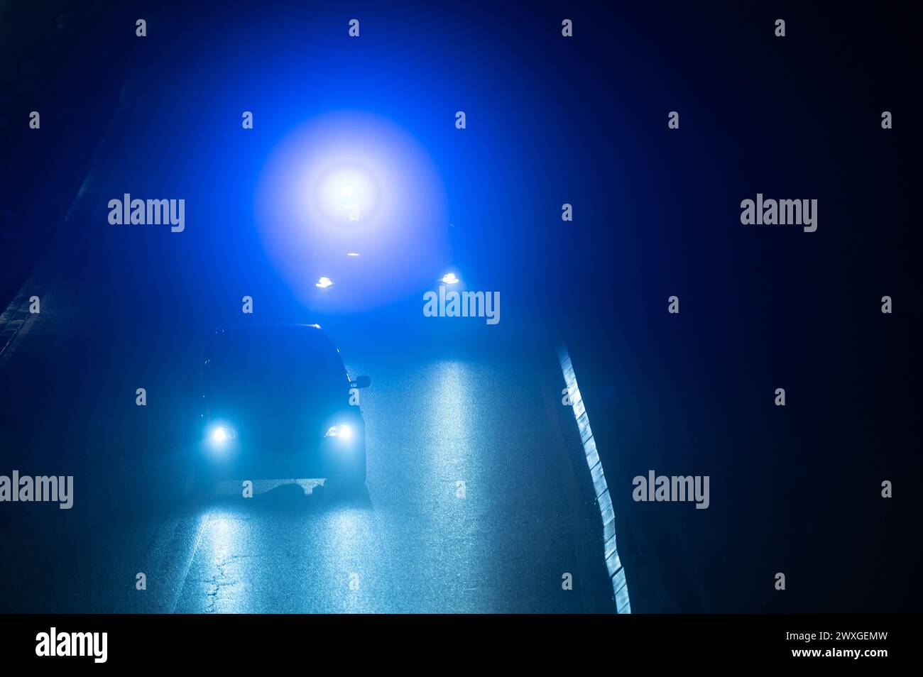 SYMBOLE - 29 mars 2024, Rhénanie-Palatinat, Nürburg : une voiture de police roule derrière un véhicule sur une route dans l'obscurité avec des feux bleus clignotants sur le "vendredi voiture" au Nürburgring. Car Friday' est l'ouverture de la saison pour les fans de voitures. Photo : Silas Stein/dpa Banque D'Images