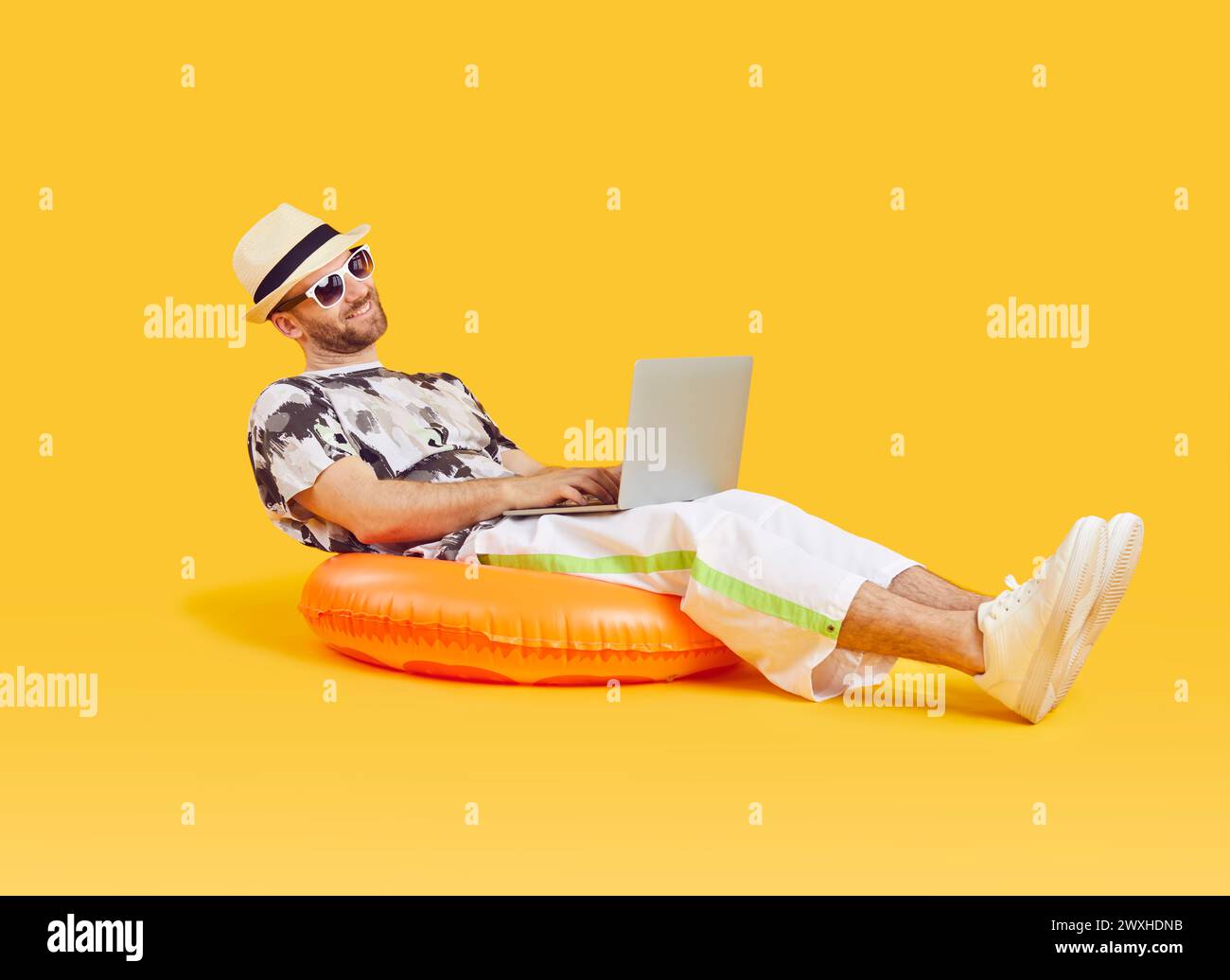 Heureux homme d'affaires travaillant sur ordinateur portable tout en se relaxant sur anneau de natation pendant les vacances d'été Banque D'Images