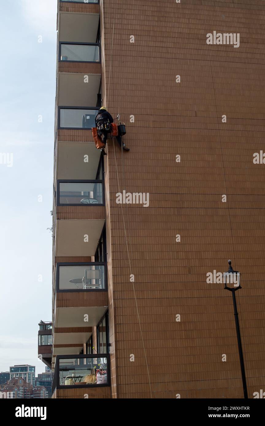 Vauxhall, Londres, Royaume-Uni. 26 mars 2024. Un entrepreneur avec une tête pour les hauteurs pend à un bloc d'appartements à côté du pont Vauxhall pour faire l'entretien. Crédit : Maureen McLean/Alamy Banque D'Images