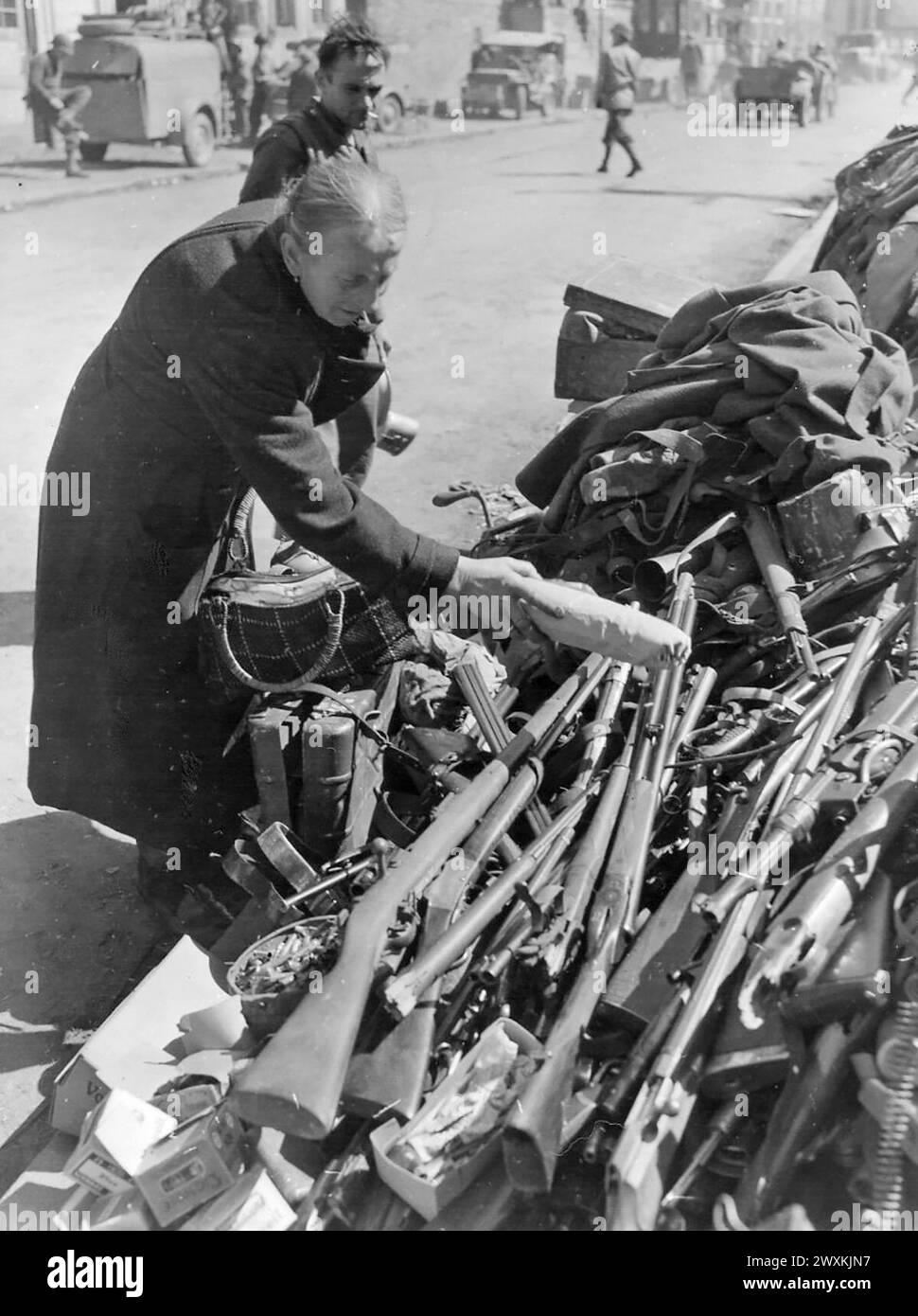 Femme âgée place un paquet sur une pile d'armes à Rubeland, Allemagne CA. Avril 1945 Banque D'Images