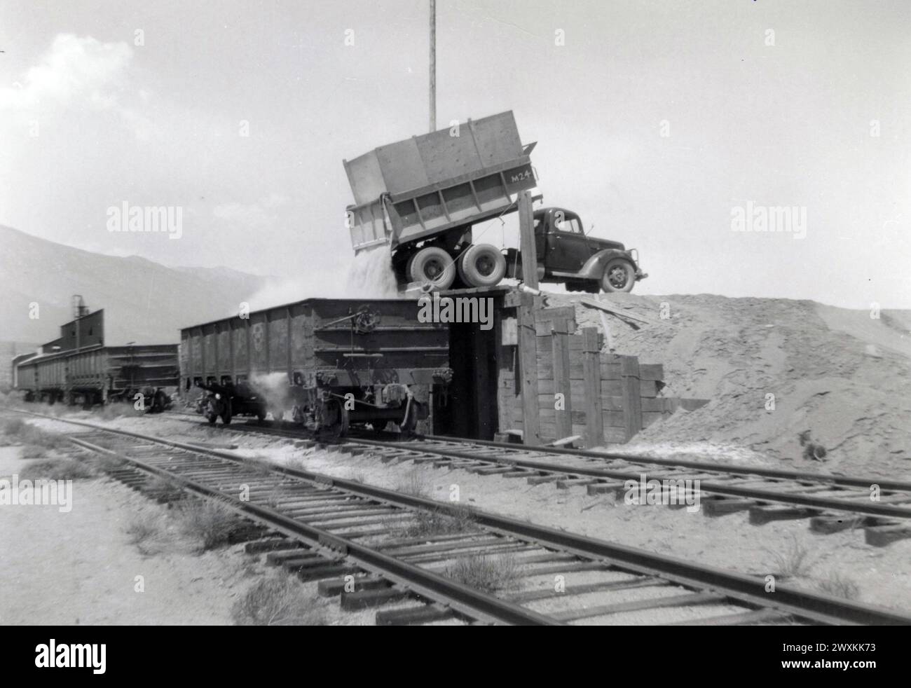 Un camion à benne basculante utilisé pour charger des wagons à Sykes Siding sur terre condamné pour la construction de la Naval Air Weapons Station, China Lake dans le comté d'Inyo en Californie, usine de traitement dans le fond CA. 1946-1947 Banque D'Images