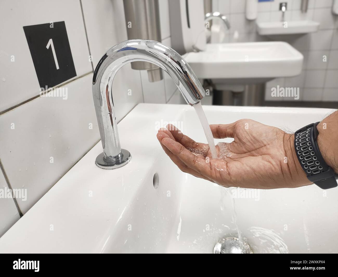 Gros plan d'un homme se lave les mains à l'aide d'un robinet sans contact. Banque D'Images