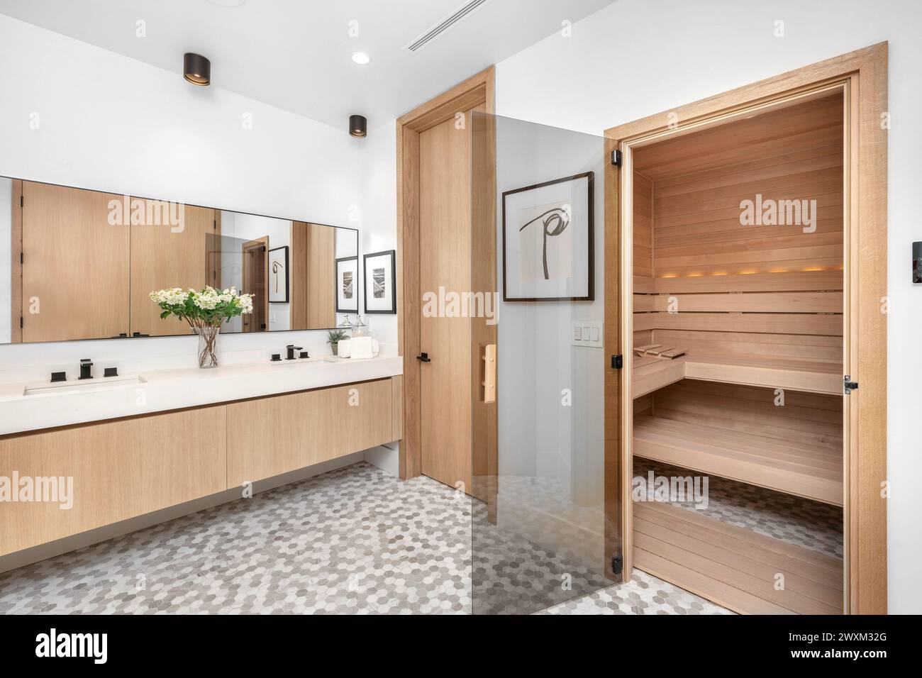 Une salle de bains moderne avec des armoires en bois spacieuses, des comptoirs blancs et un lavabo double. Banque D'Images