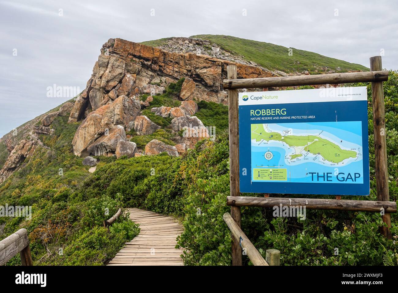 Vue panoramique sur la réserve naturelle de Robberg avec un sentier menant aux falaises rocheuses et un panneau détaillant le sentier de randonnée 'The Gap' en Afrique du Sud. Banque D'Images