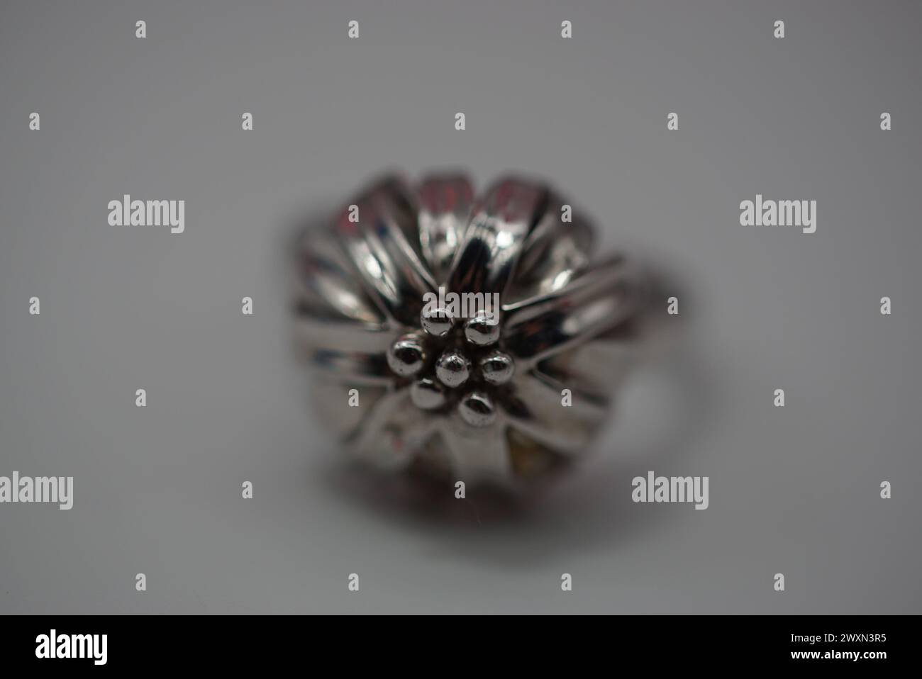 Une bague en argent avec un motif floral complexe affiché sur une surface de table blanche et propre Banque D'Images