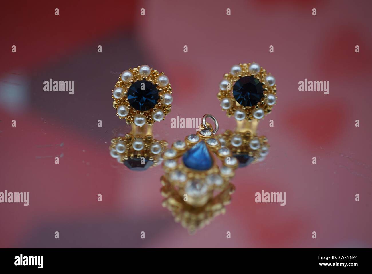 Une boucle d'oreille en or ornée de diamants bleus et de perles sur fond rose Banque D'Images