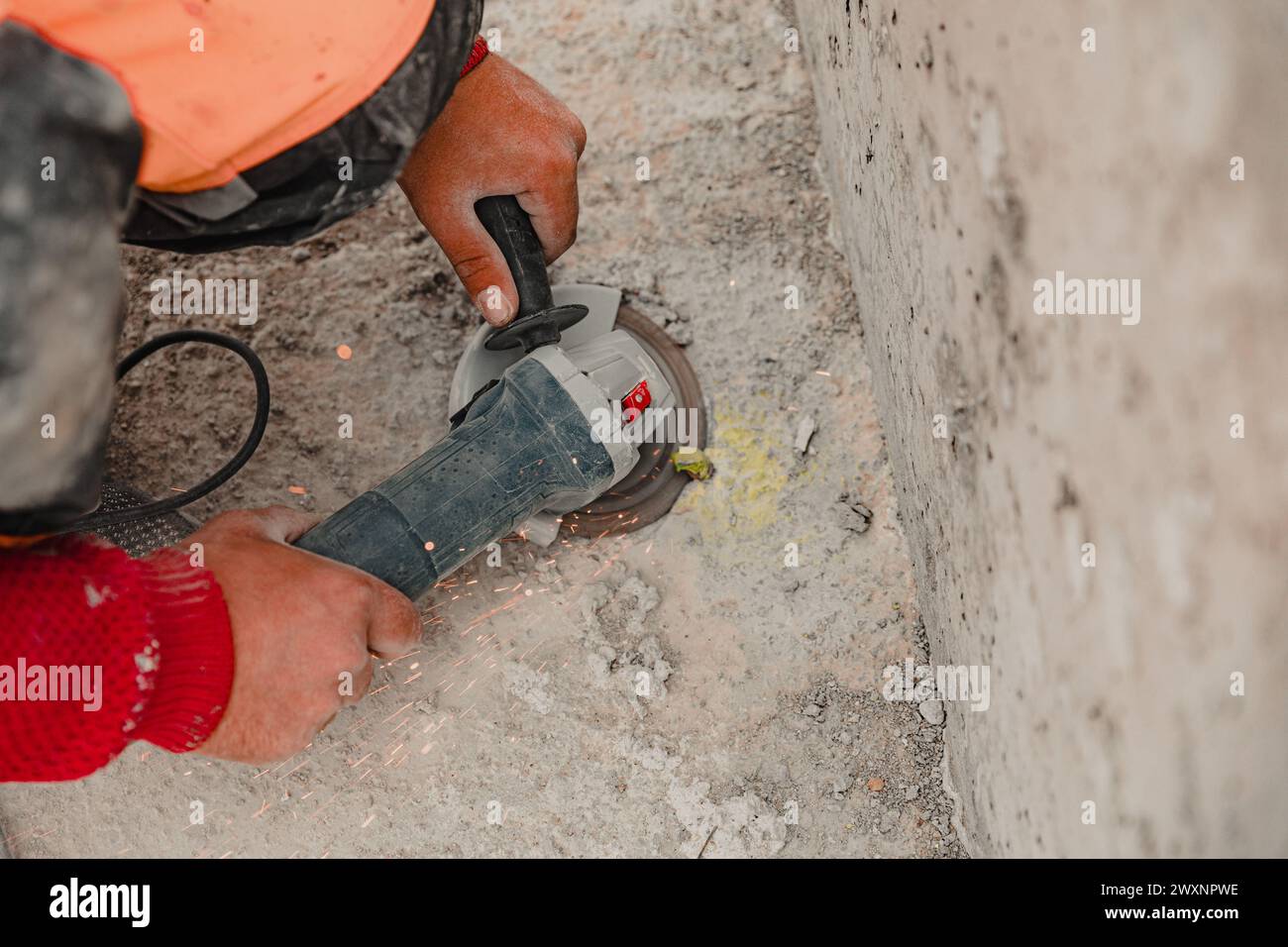 Un ouvrier de la construction en chemise orange utilisant un outil rotatif sur un mur de ciment Banque D'Images