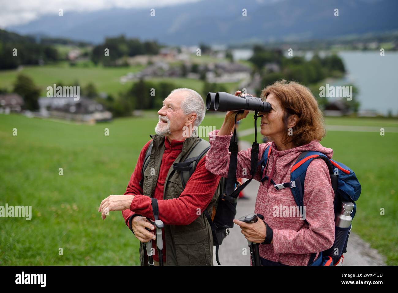 Couple âgé actif randonnée ensemble dans les montagnes d'automne. Les touristes seniors appréciant la nature regardent à travers des jumelles. Banque D'Images