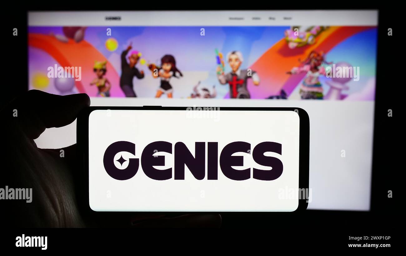 Personne tenant le téléphone portable avec le logo de la société de technologie avatar US Genies Inc en face de la page Web de l'entreprise. Concentrez-vous sur l'affichage du téléphone. Banque D'Images