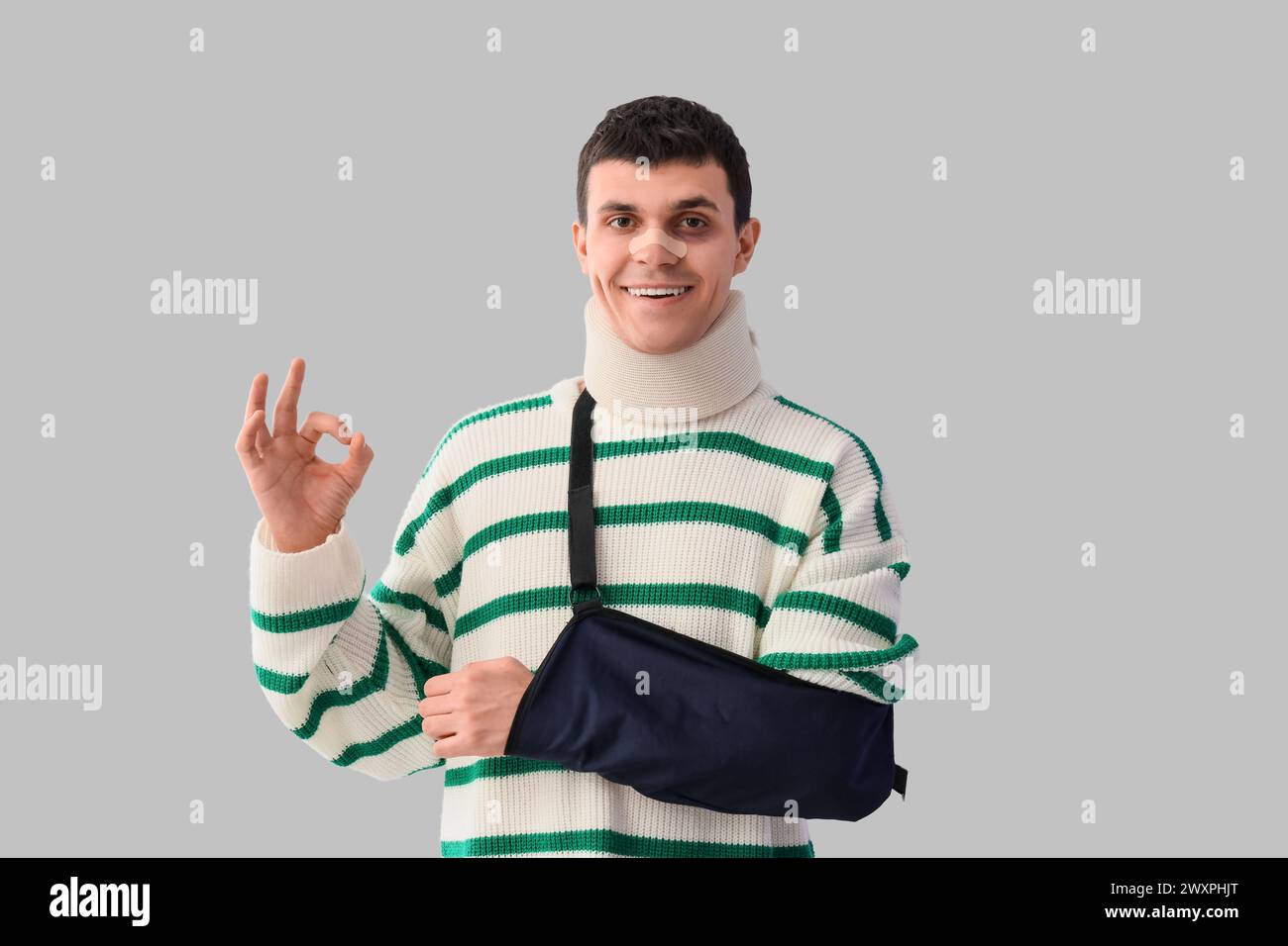 Jeune homme blessé après un accident avec bras cassé montrant OK sur fond clair Banque D'Images