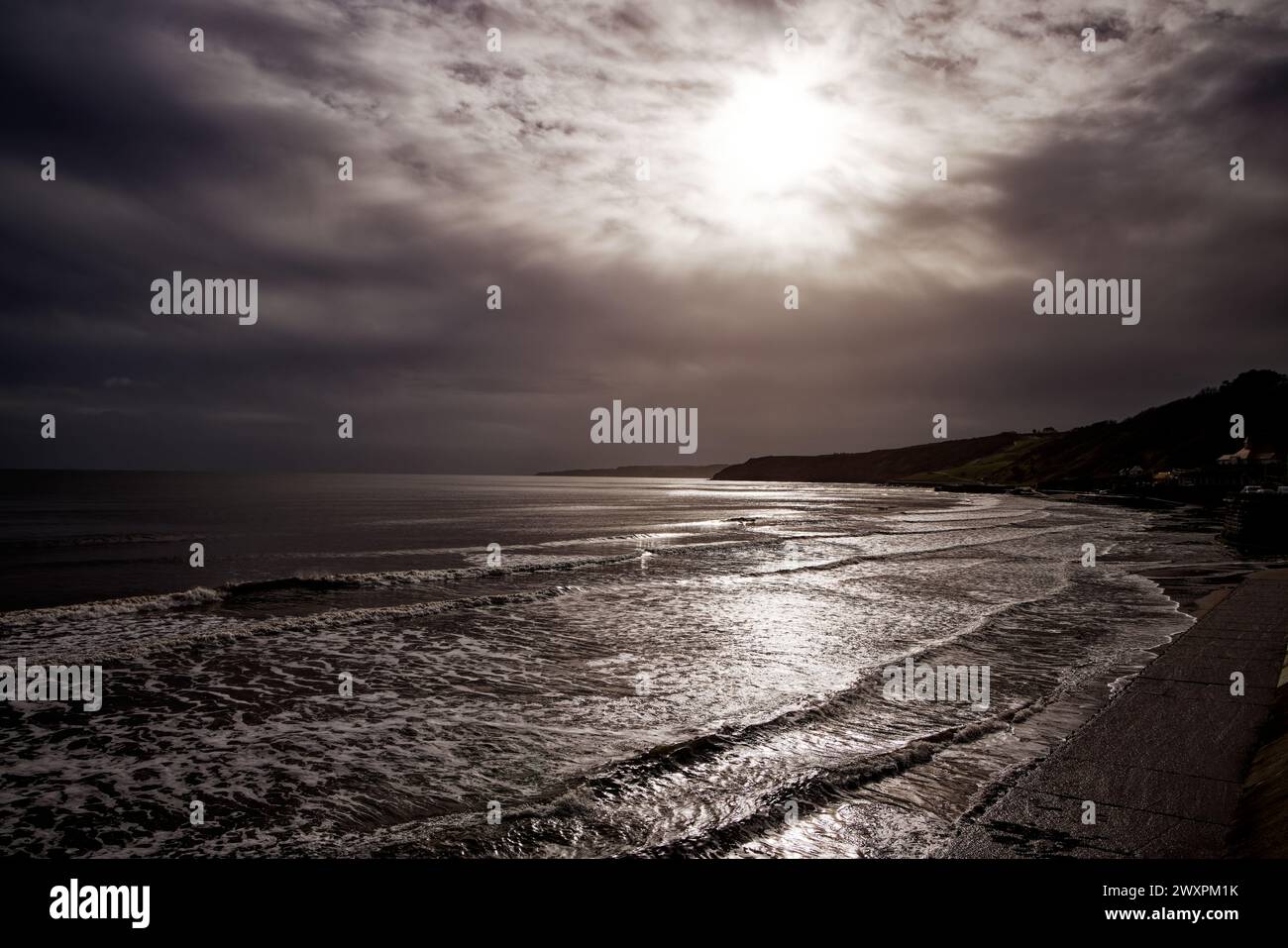 La lumière du soleil éclate à travers les nuages gris pluvieux et brille à travers les vagues qui courent sur une plage, Scarborough South Bay, North Yorkshire, Angleterre. Banque D'Images