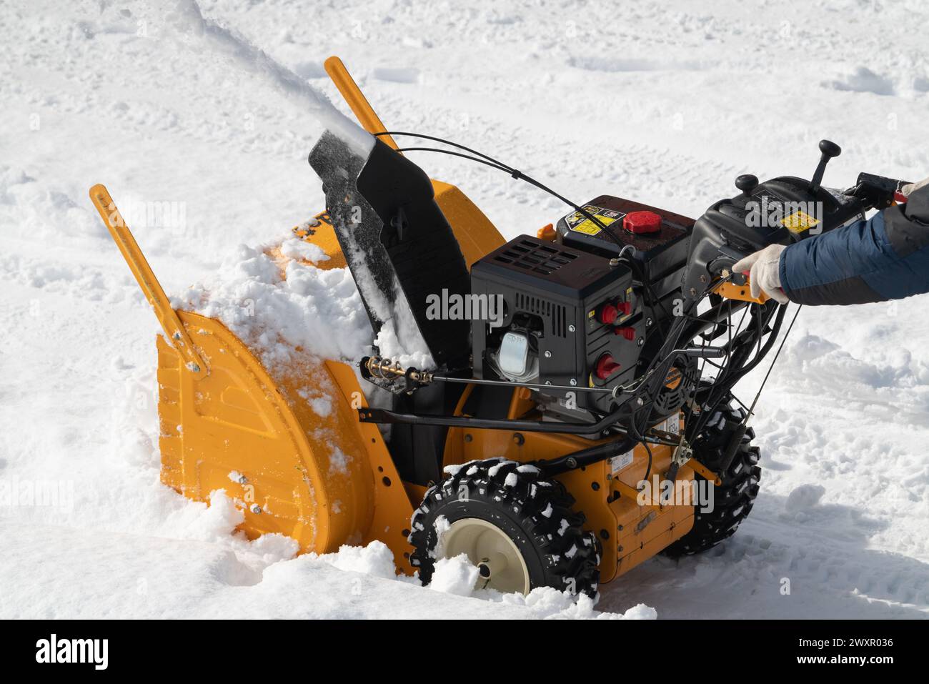 Travailleur utilisant une souffleuse à neige pour déneiger le stationnement après l'ouragan d'hiver. Déneigement mécanisé du trottoir, zone de déneigement par jour ensoleillé Banque D'Images