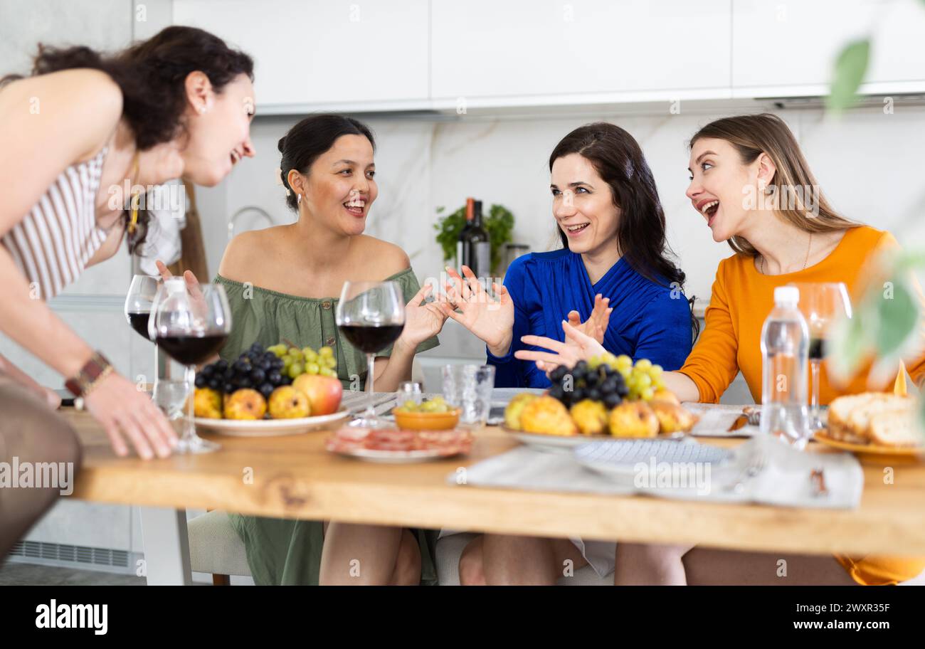 Des femmes heureuses se sont rassemblées autour d’une table festive, participant à des discussions animées et profitant des délices du vin Banque D'Images